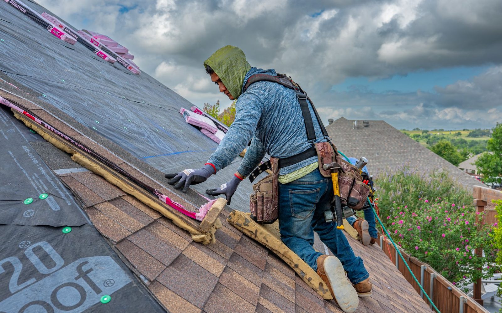 Roofers installing shingles on a house under a clear sky