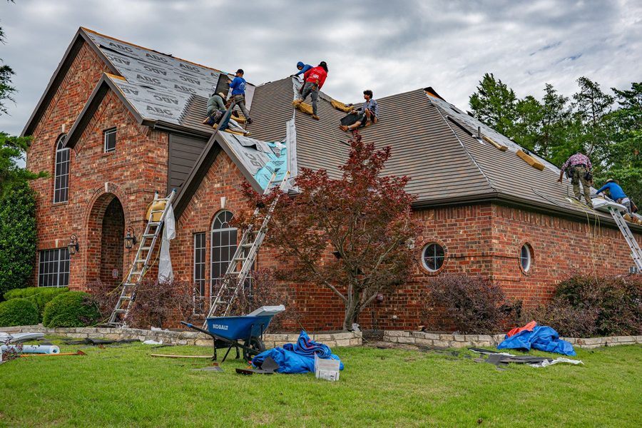 Crew working on a shingle roof of a brick house